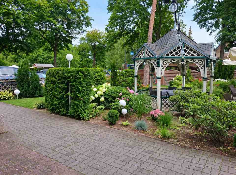 Der Hotelgarten mit hölzernem Pavillon, Hecken und blühenden Sträuchern